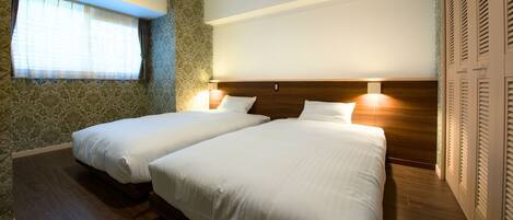 A hotel room with two beds, a window with curtains, patterned wallpaper, and a wooden headboard.