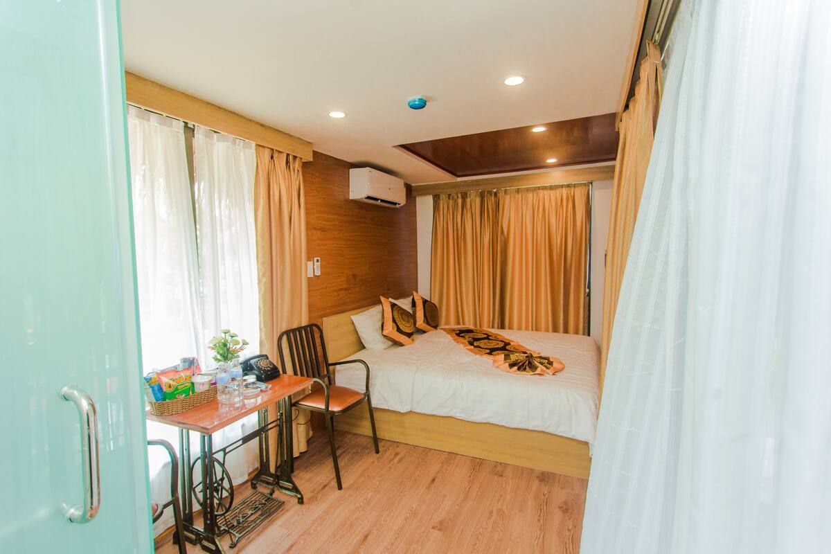 A hotel room with a bed, a desk, a chair, and an air conditioning unit.