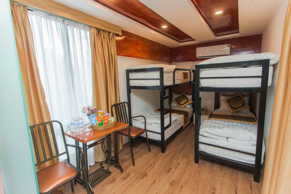 A bunk bed room with a wooden table and chairs, a window with curtains, and an air conditioning unit on the wall.