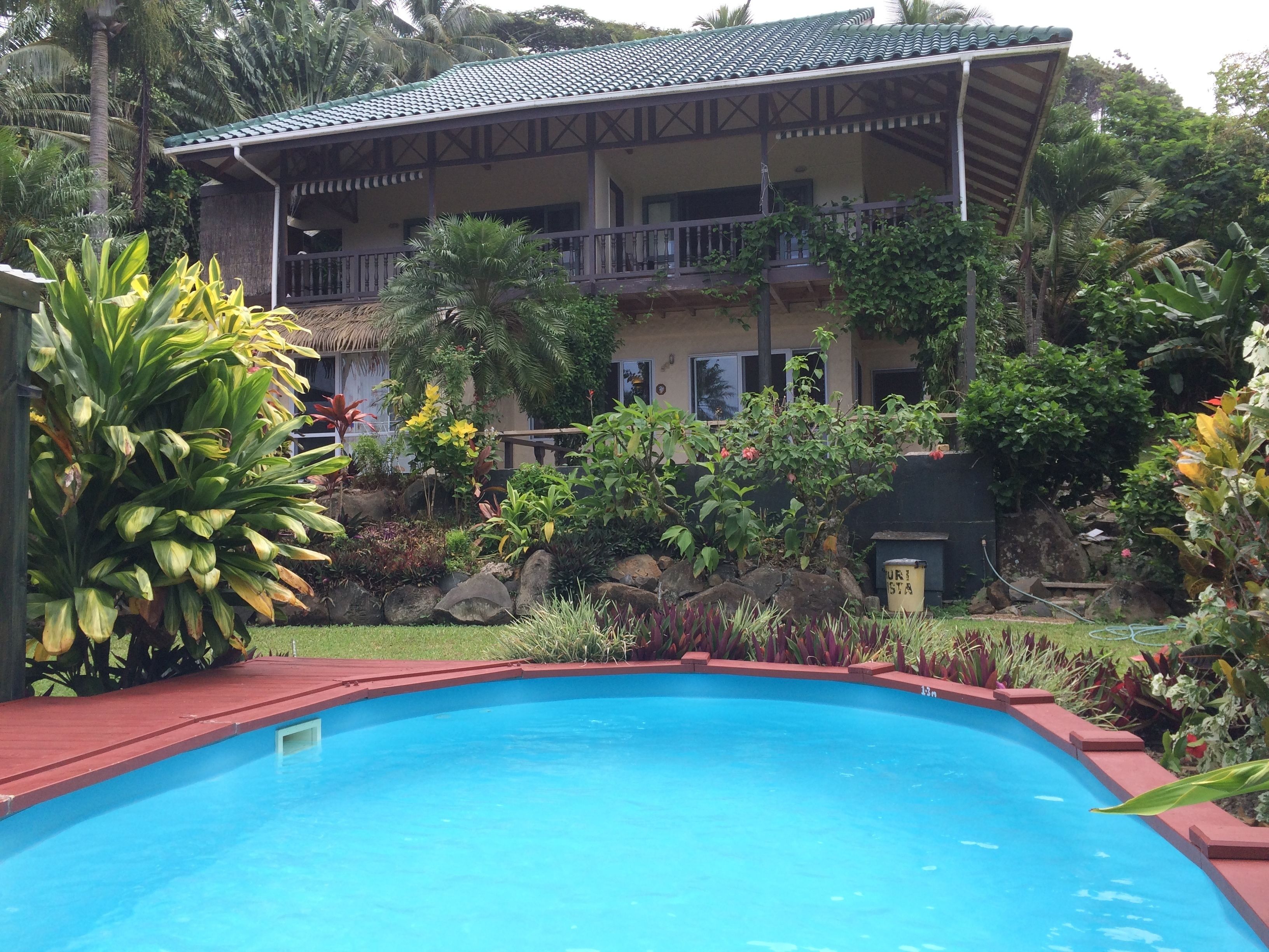 Une piscine entourée de plantes tropicales et un bâtiment doté d’un toit en tuiles et de balcons.