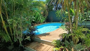 Ein Garten mit einer Holzterrasse und einem Schwimmbad, umgeben von üppiger Bepflanzung.