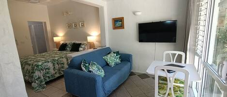 Ein Zimmer mit einem Bett, einem blauen Sofa, einem Fernseher und einem Fenster mit Jalousien.