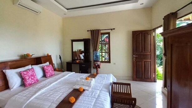 Een slaapkamer met een groot bed, een houten hoofdbord, een nachtkastje, een dressoir, een spiegel en een raam met gordijnen.