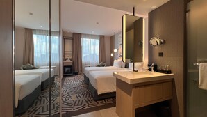 Habitación de hotel con dos camas, un espejo grande, un lavamanos y una alfombra estampada.