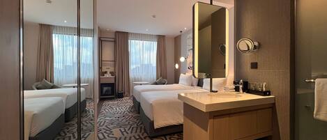 Habitación de hotel con dos camas, un espejo grande, un lavamanos y una alfombra estampada.