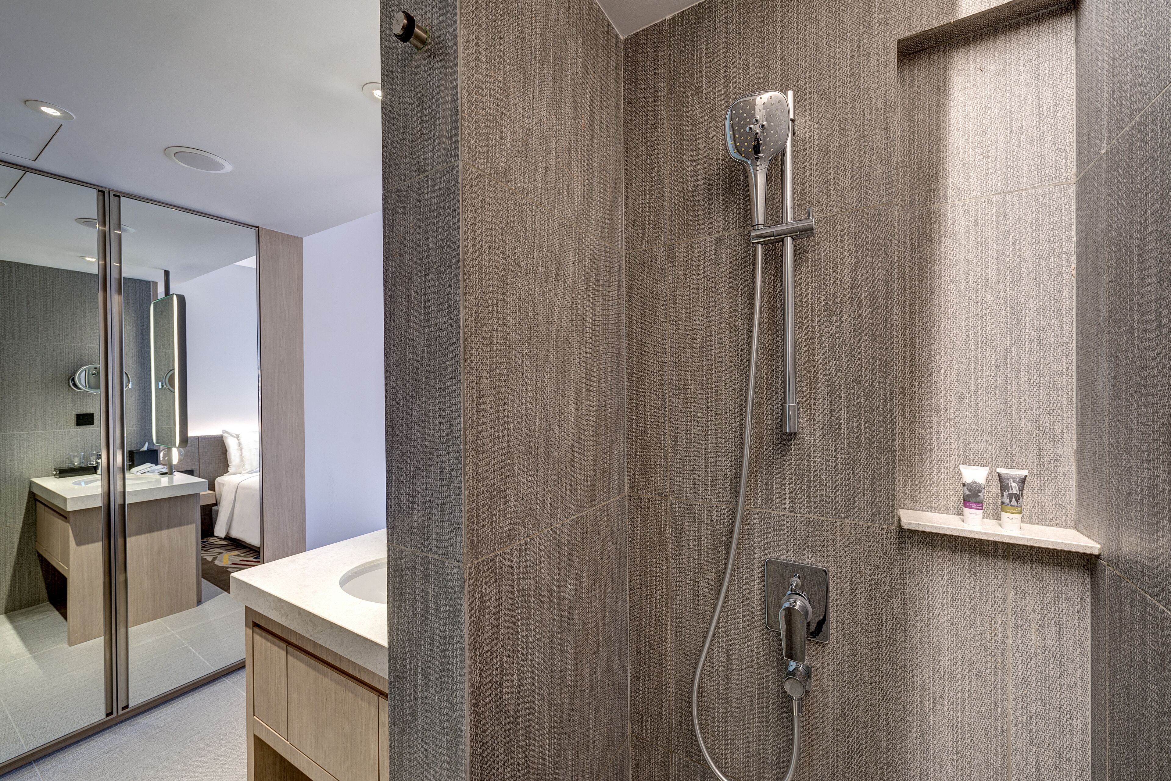 A modern bathroom with a shower, a vanity with a mirror, and a small shelf with toiletries.