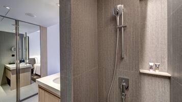 A modern bathroom with a shower, a vanity with a mirror, and a small shelf with toiletries.