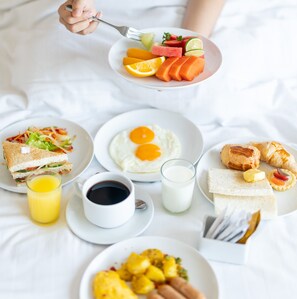 Un desayuno servido sobre una cama, con varios platos que incluyen huevos, tostadas y fruta.