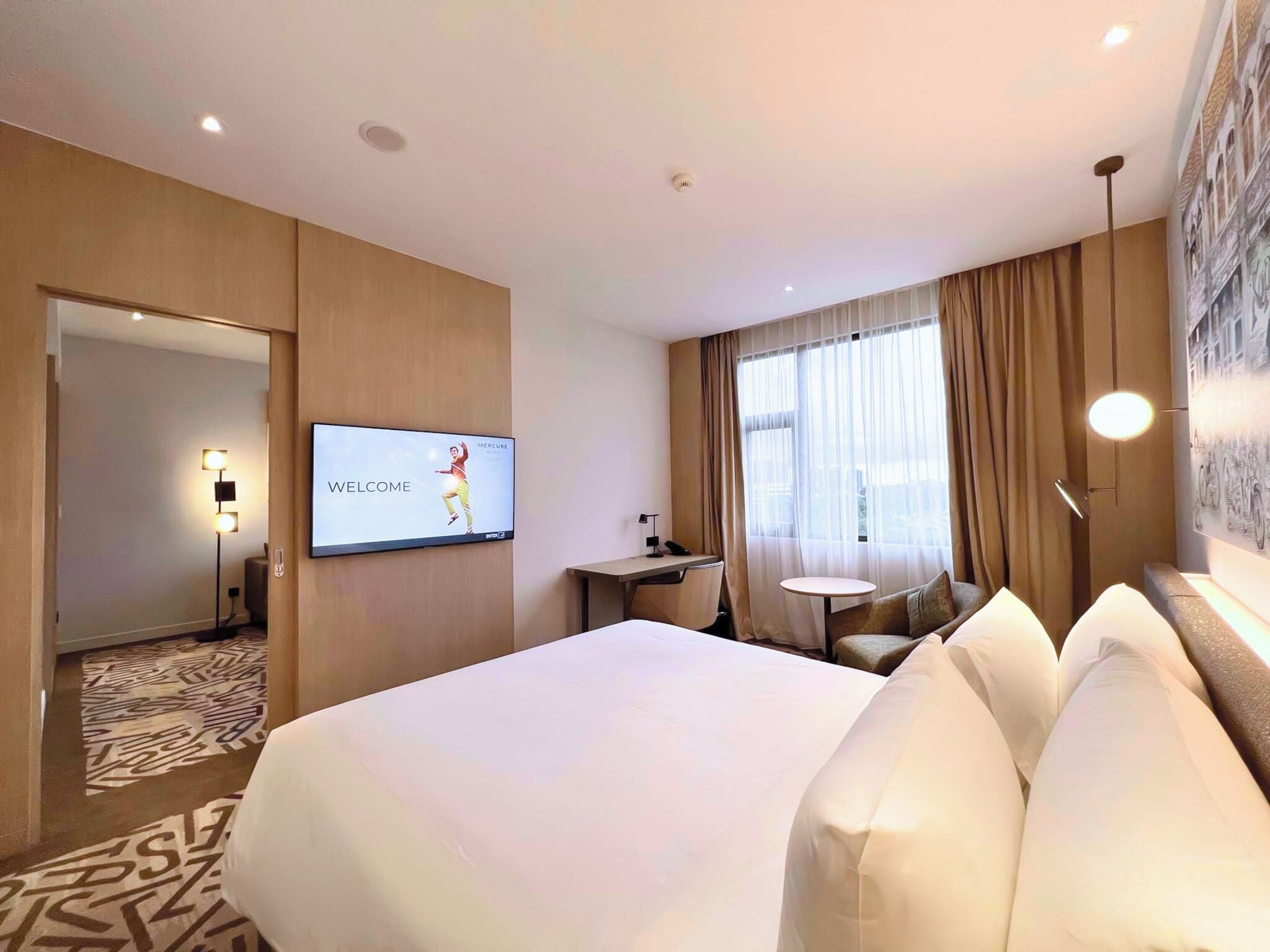 Una habitación de hotel con una cama grande, un escritorio, una silla, un televisor y una ventana con cortinas.