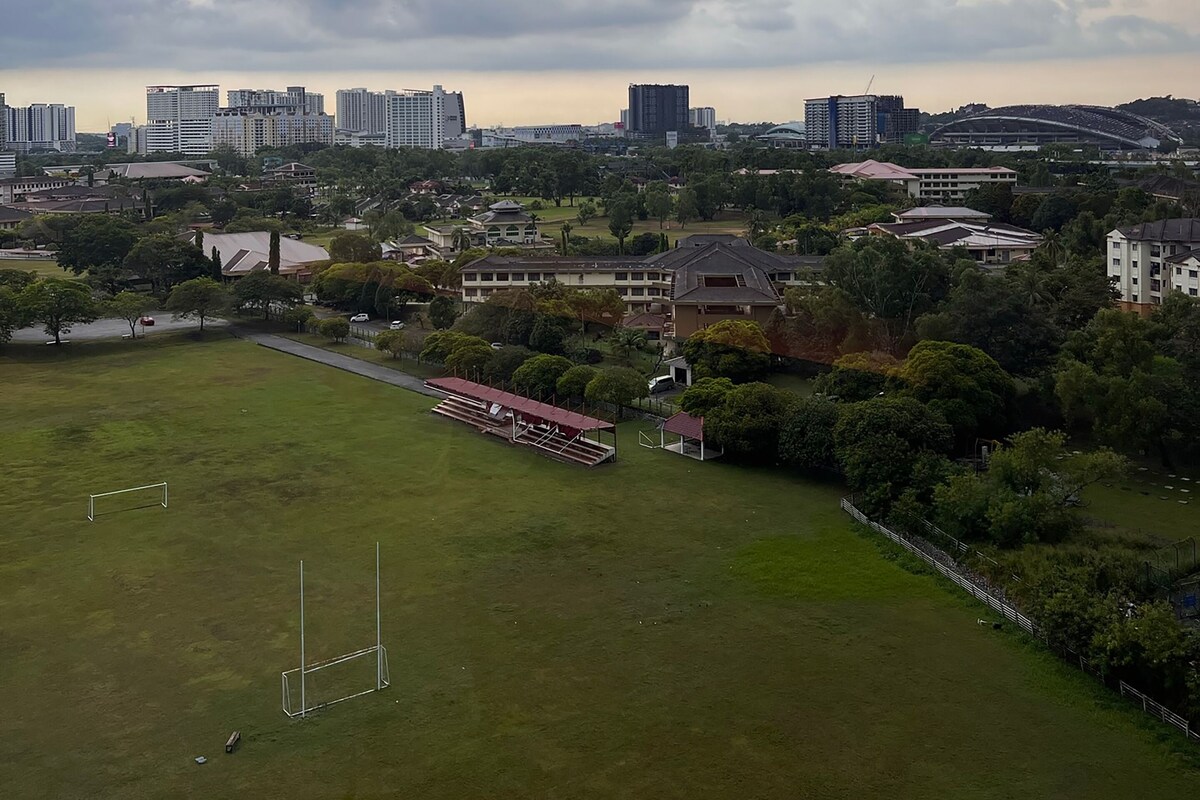 Eine Stadtansicht mit einem großen Grünpark, einem Fußballplatz und verschiedenen Gebäuden, darunter Hochhauswohnungen und ein Stadion.