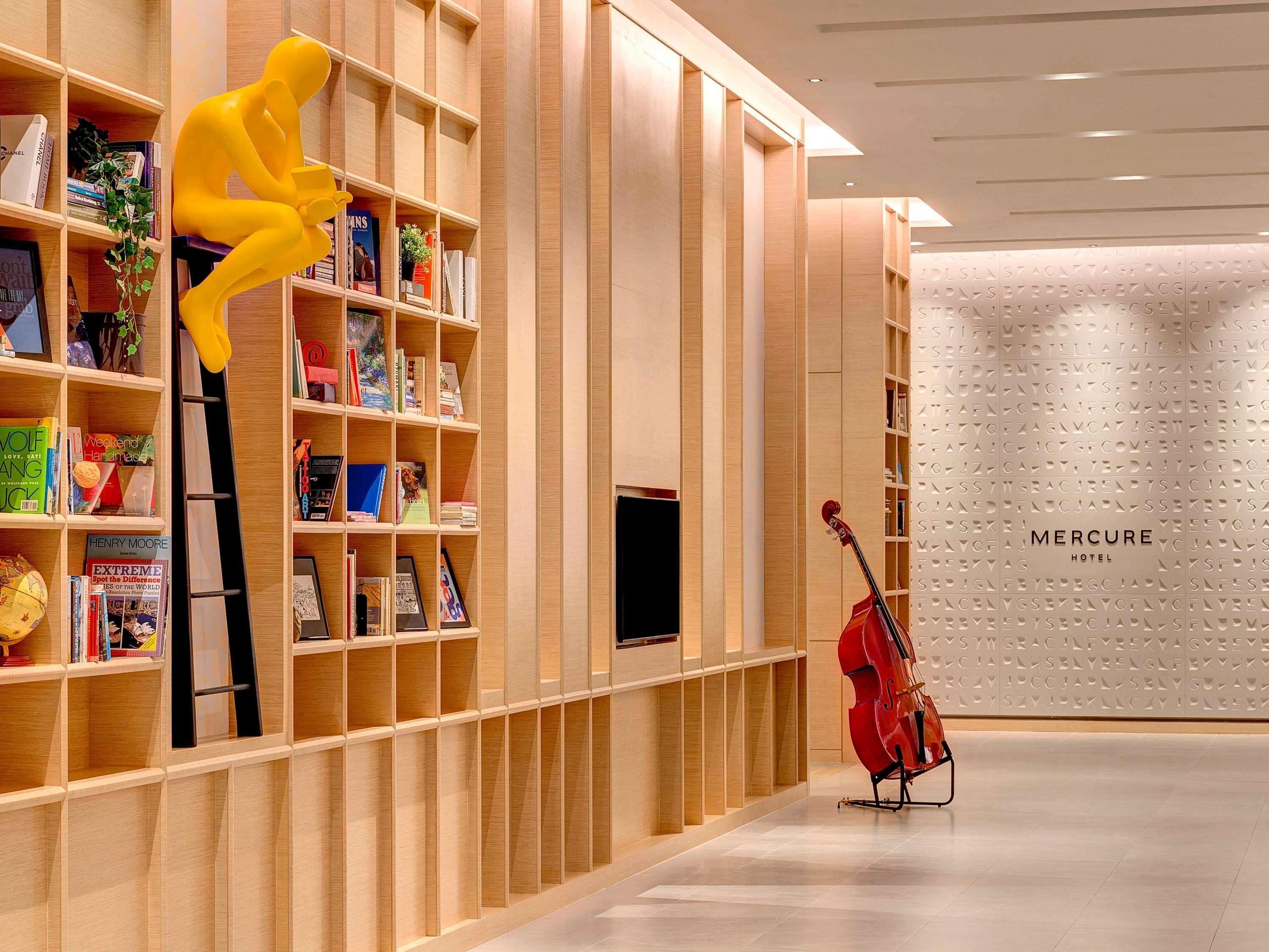 Un interior de hotel moderno con estanterías de madera, un violonchelo rojo y una escultura amarilla.