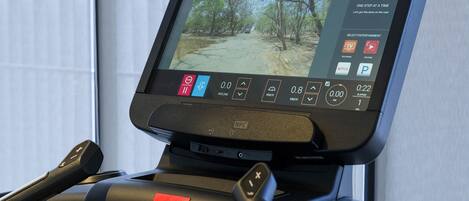 A treadmill with a digital display, control panel, and a red emergency stop button.