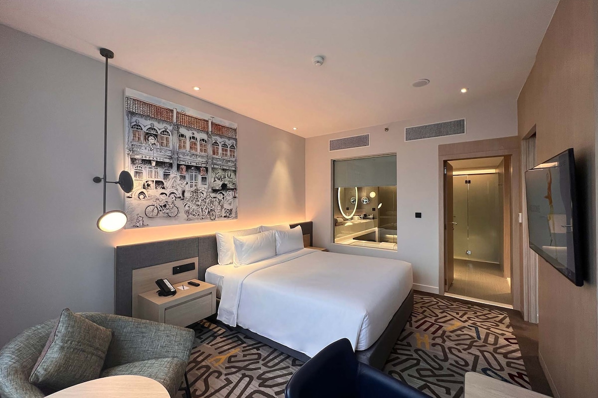 Ein Hotelzimmer mit einem großen Bett, einem Schreibtisch, einem Sessel, einer Couch, einem wandmontierten Fernseher und einem Badezimmer mit Spiegel und Waschbecken.