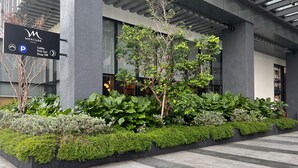 Un moderno vestíbulo de hotel con un letrero negro que indica una zona de estacionamiento, un punto de recogida/devolución en el vestíbulo y un jardín con diversas arbustos y árboles.