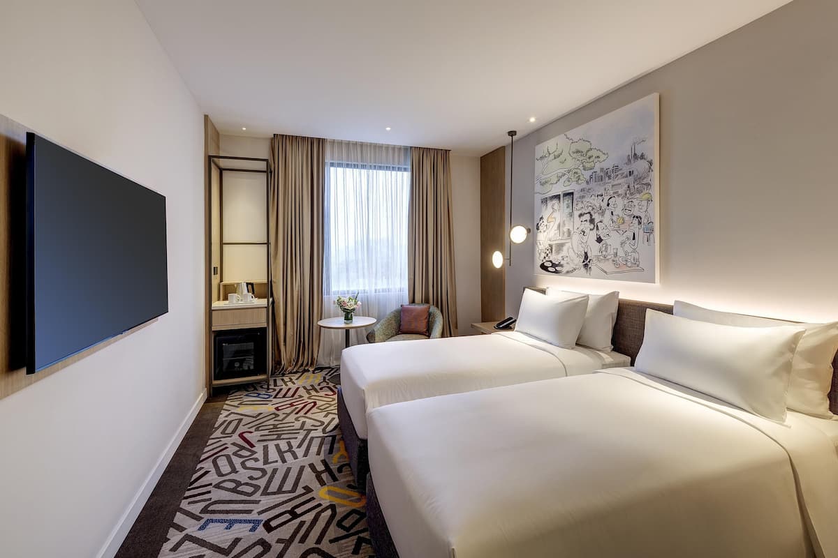 A hotel room with a large bed, a desk with a chair, a small table with a vase, and a wall-mounted TV.