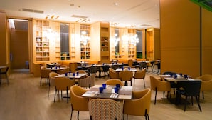 Un comedor con varias mesas y sillas, estanterías de madera y luces colgantes.