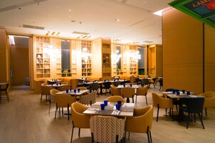 A dining area with multiple tables and chairs, wooden bookshelves, and hanging lights.