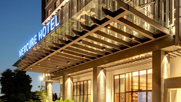 Un hotel moderno con entrada de cristal y un letrero que dice 'Mercure Hotel'.