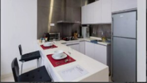 A modern kitchen with white cabinets, a stainless steel refrigerator, and a dining area with a table set for two. - Bangsar Camelia Homestay KL (Kuala Lumpur)