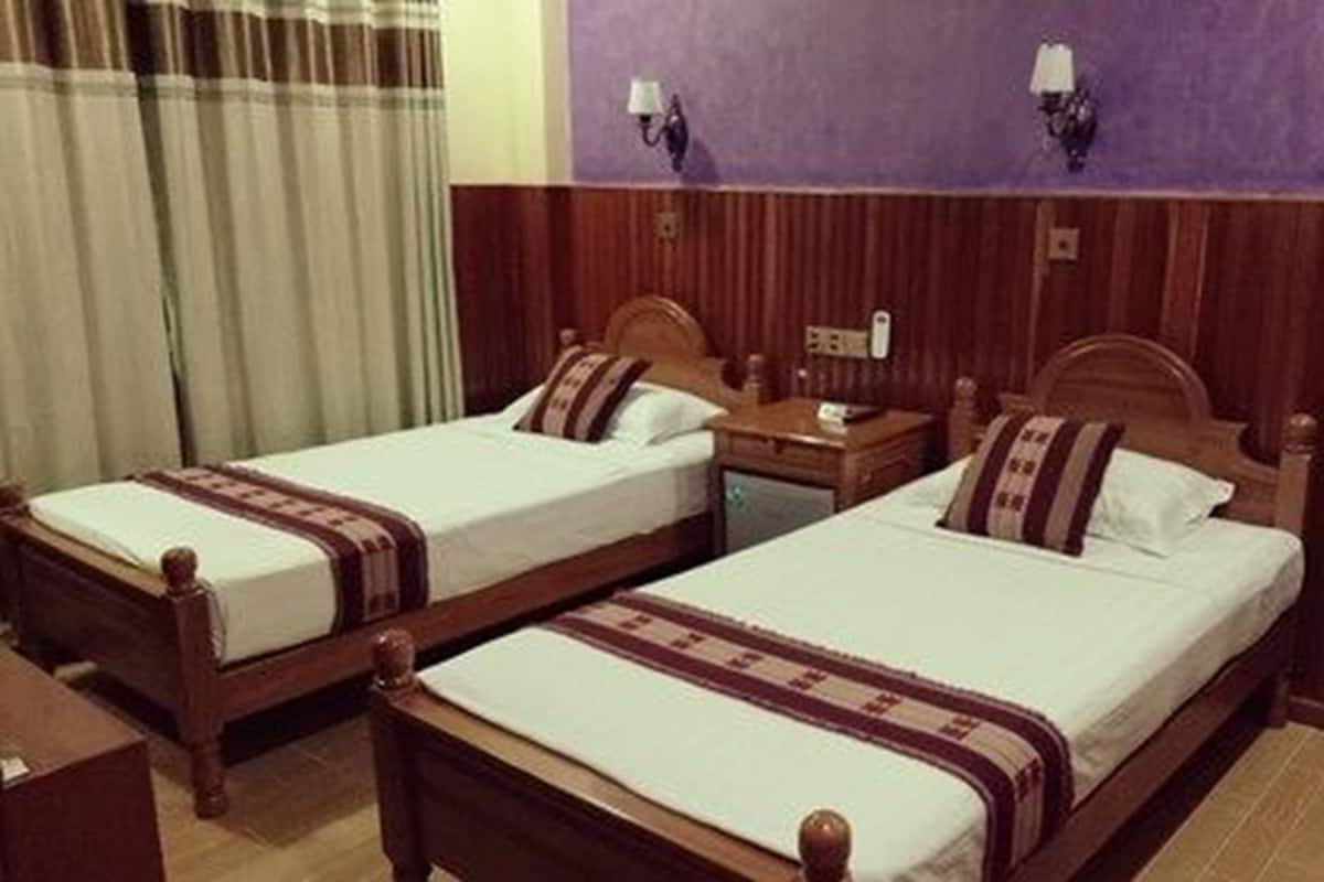 Two single beds with wooden headboards, a nightstand, and a wall-mounted lamp between them.