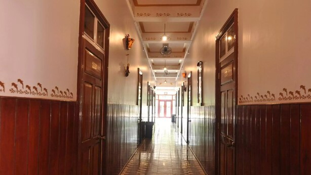 Un corridoio con porte in legno e pavimento piastrellato, che conduce a una stanza luminosa con una porta rossa in fondo.