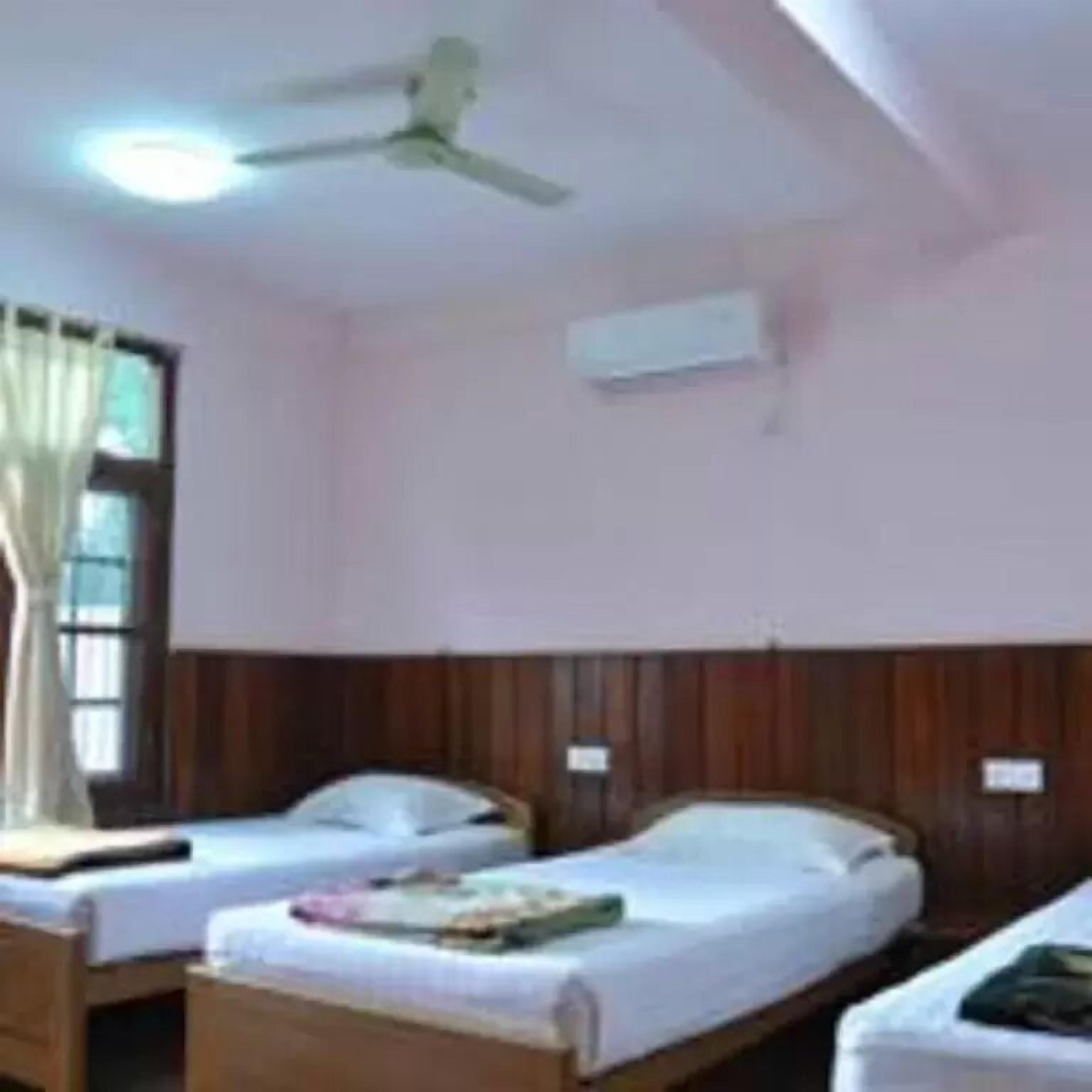A room with two single beds, a ceiling fan, an air conditioning unit, and wooden paneling on the walls.