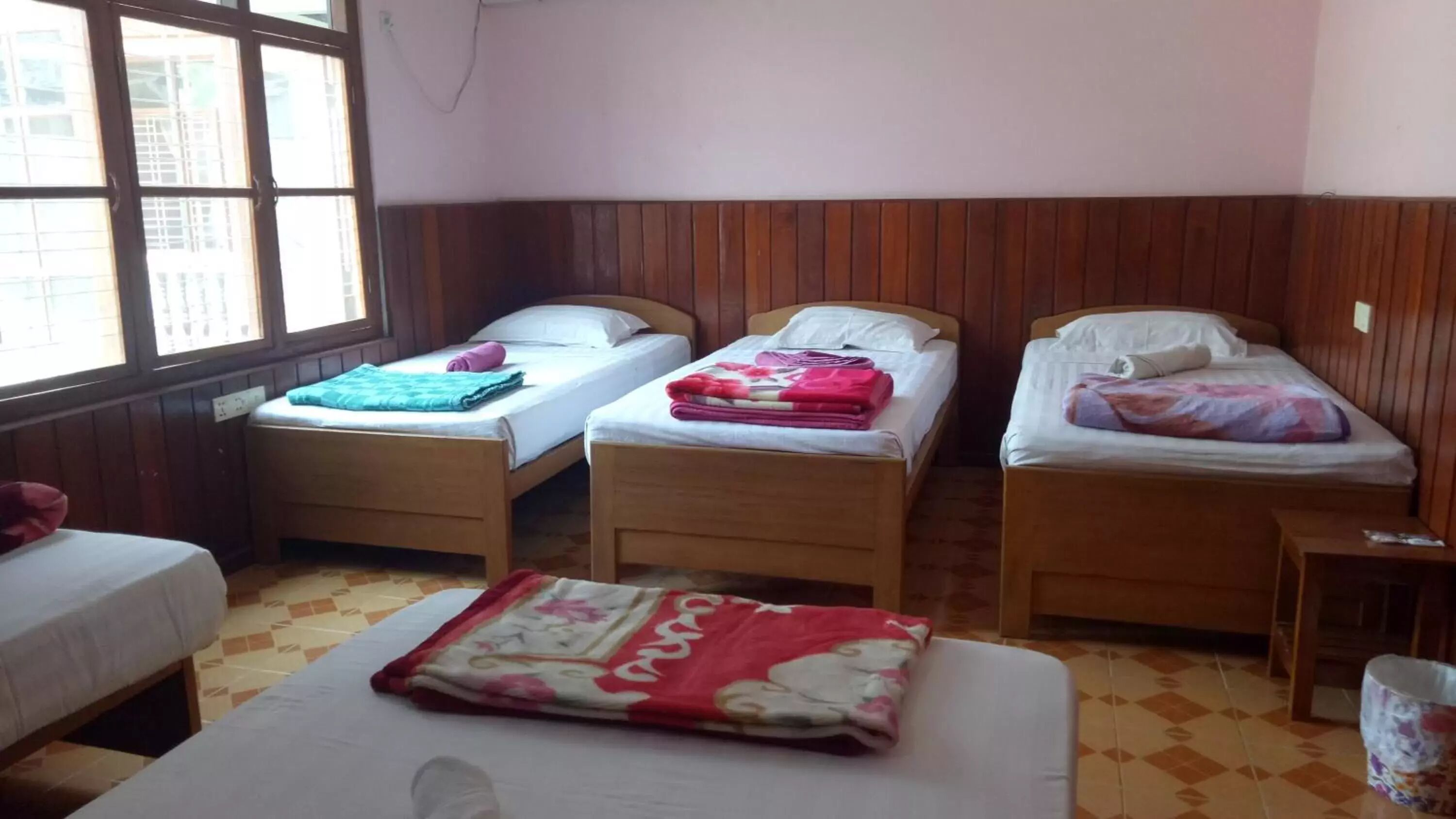 Una habitación con tres camas de madera, cada una con colchón y almohadas blancas, y una manta colorida sobre el suelo.