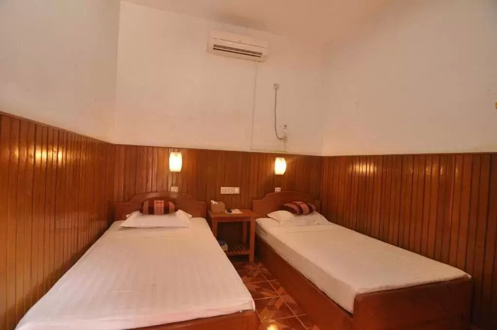 A room with two single beds, wooden paneling on the walls, and a small table between the beds.