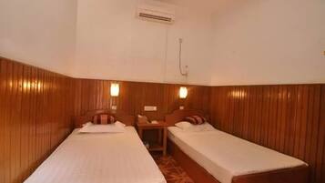 A room with two single beds, wooden paneling on the walls, and a small table between the beds.