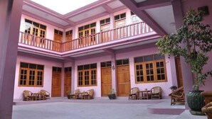 Un edificio a più piani con facciata rosa, porte in legno e un balcone con mobili in vimini.