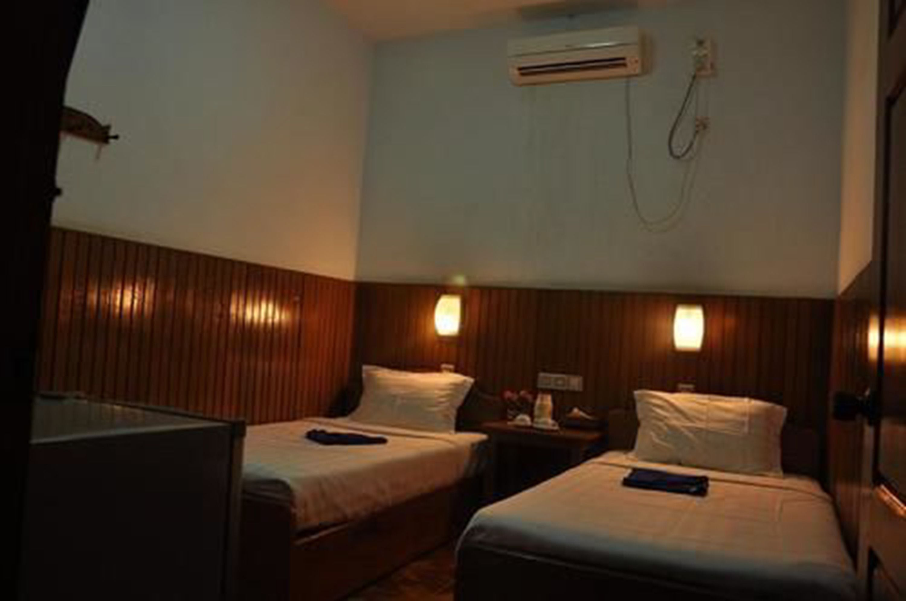 Een hotelkamer met twee bedden, houten lambrisering op de wanden, een airconditioningsapparaat en een nachtkastje met een lamp.
