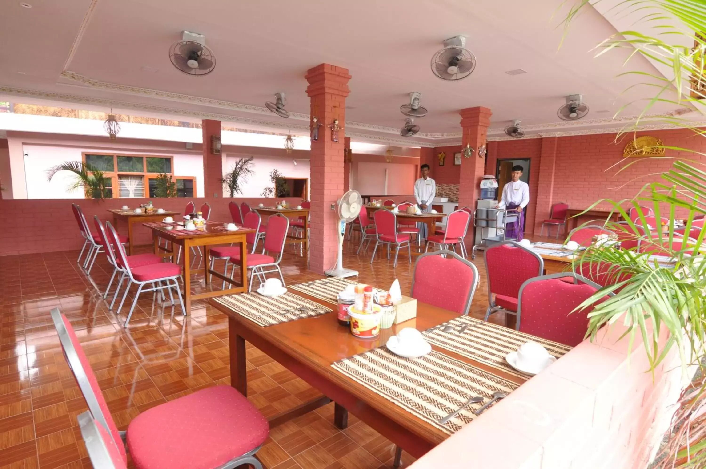 Un comedor con sillas rojas, mesas de madera y ventiladores de techo.