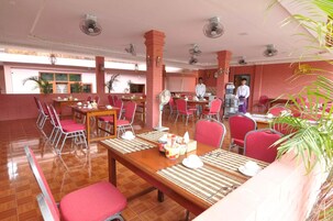 Un comedor con sillas rojas, mesas de madera y ventiladores de techo.