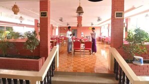 Un'ampia sala ristorante con pilastri in mattoni rossi, pavimento piastrellato e numerosi tavoli e sedie.