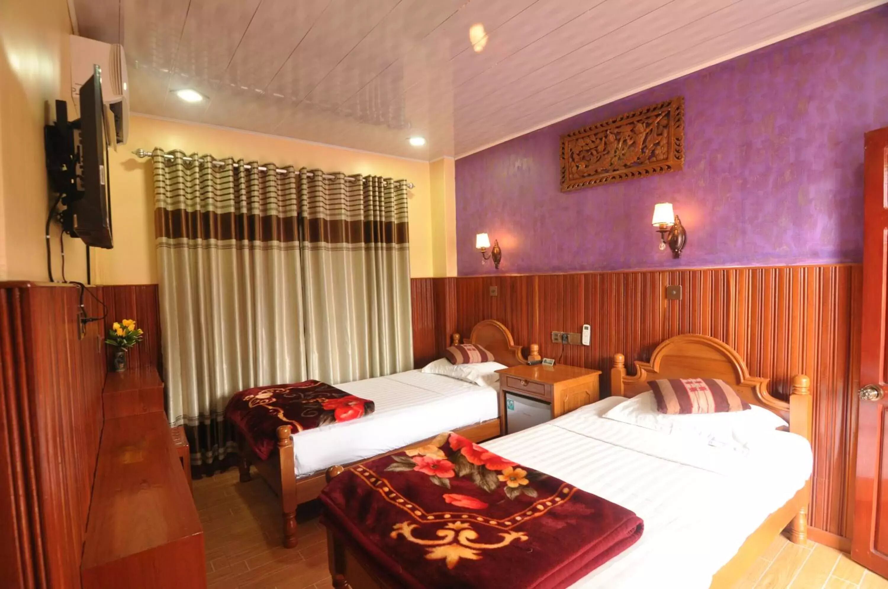 A hotel room with two beds, wooden paneling, a flat-screen TV, and a decorative wall piece.