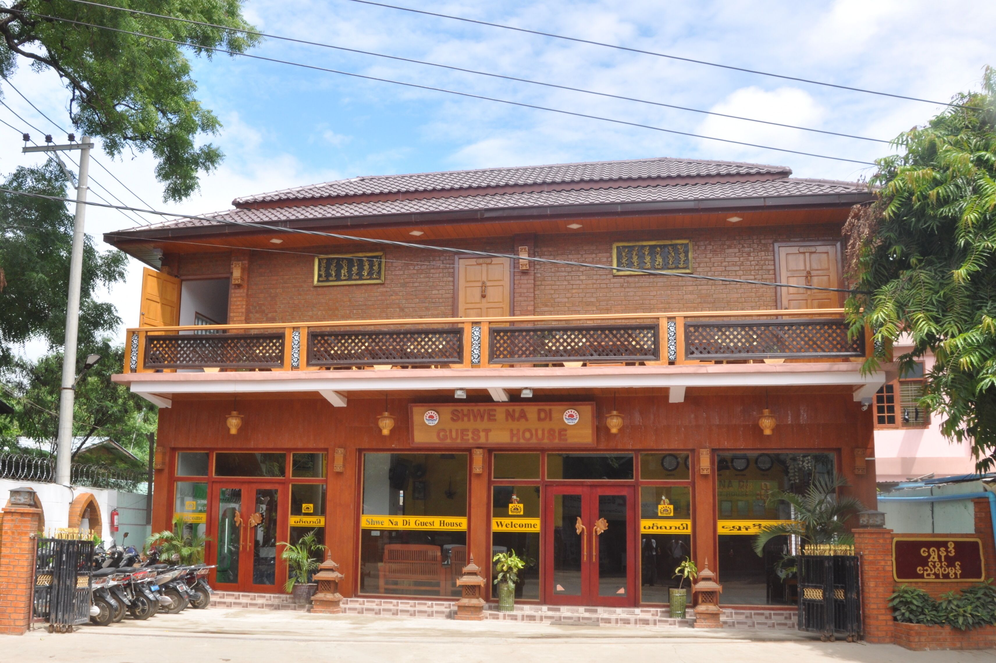 A two-story building with a sign reading "SHWE NA DI GUEST HOUSE".
