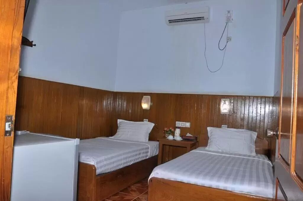 A small room with two wooden beds, a small table, and an air conditioning unit on the wall.