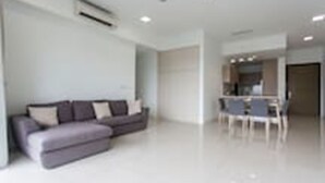 A modern living room with a grey sofa, a dining area with a table and chairs, and a kitchen in the background. - Pipit Homestay at Element Ampang (Kuala Lumpur)