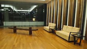 A spacious room with a wooden floor, a sofa, a bench, and a large window with vertical blinds. - Pipit Homestay at Element Ampang (Kuala Lumpur)
