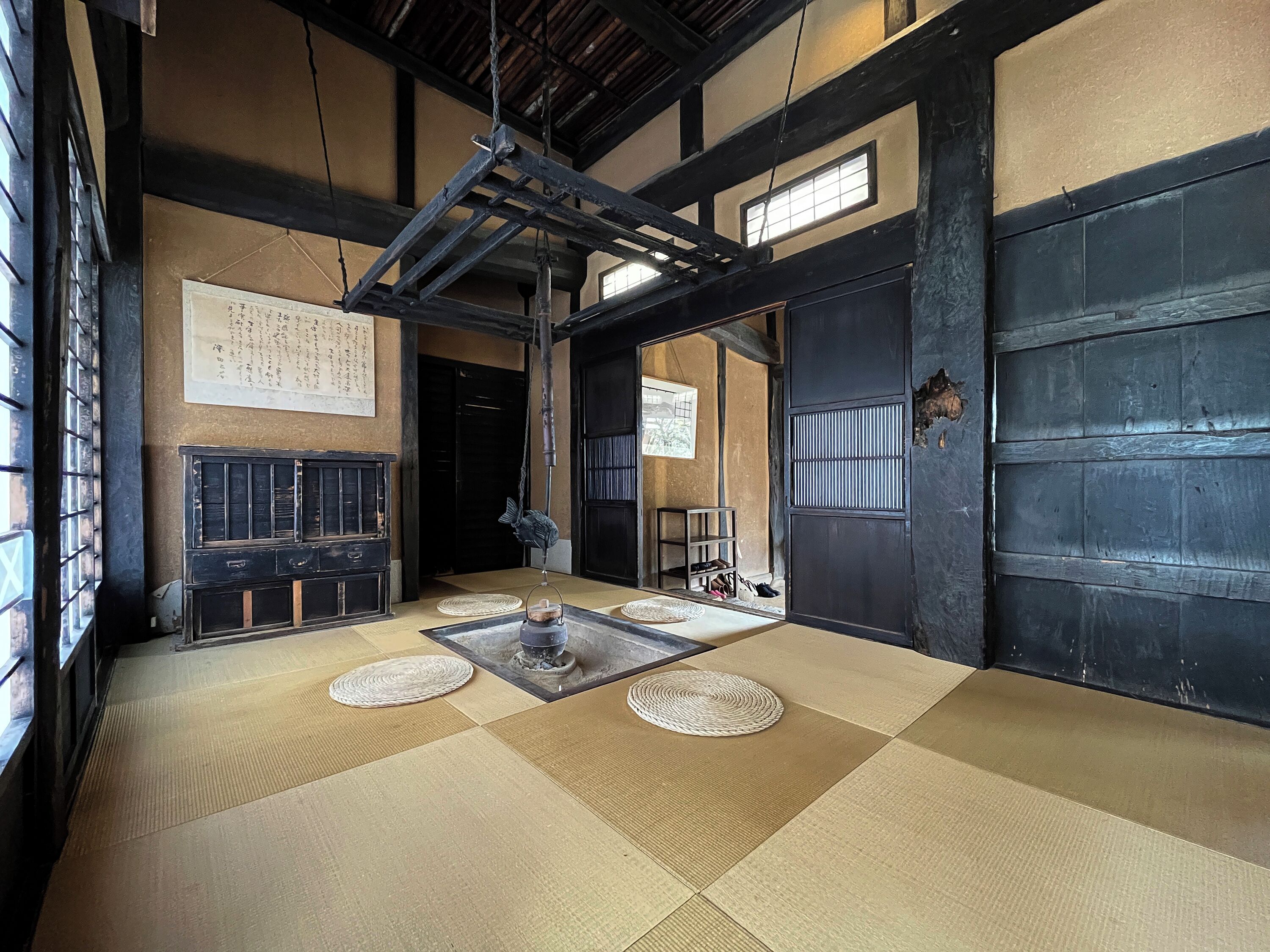 Ein traditioneller Raum mit Tatami-Matten, einer Holzbalkendecke, einer schwarzen Tür und einem kleinen Tisch mit Teeservice.