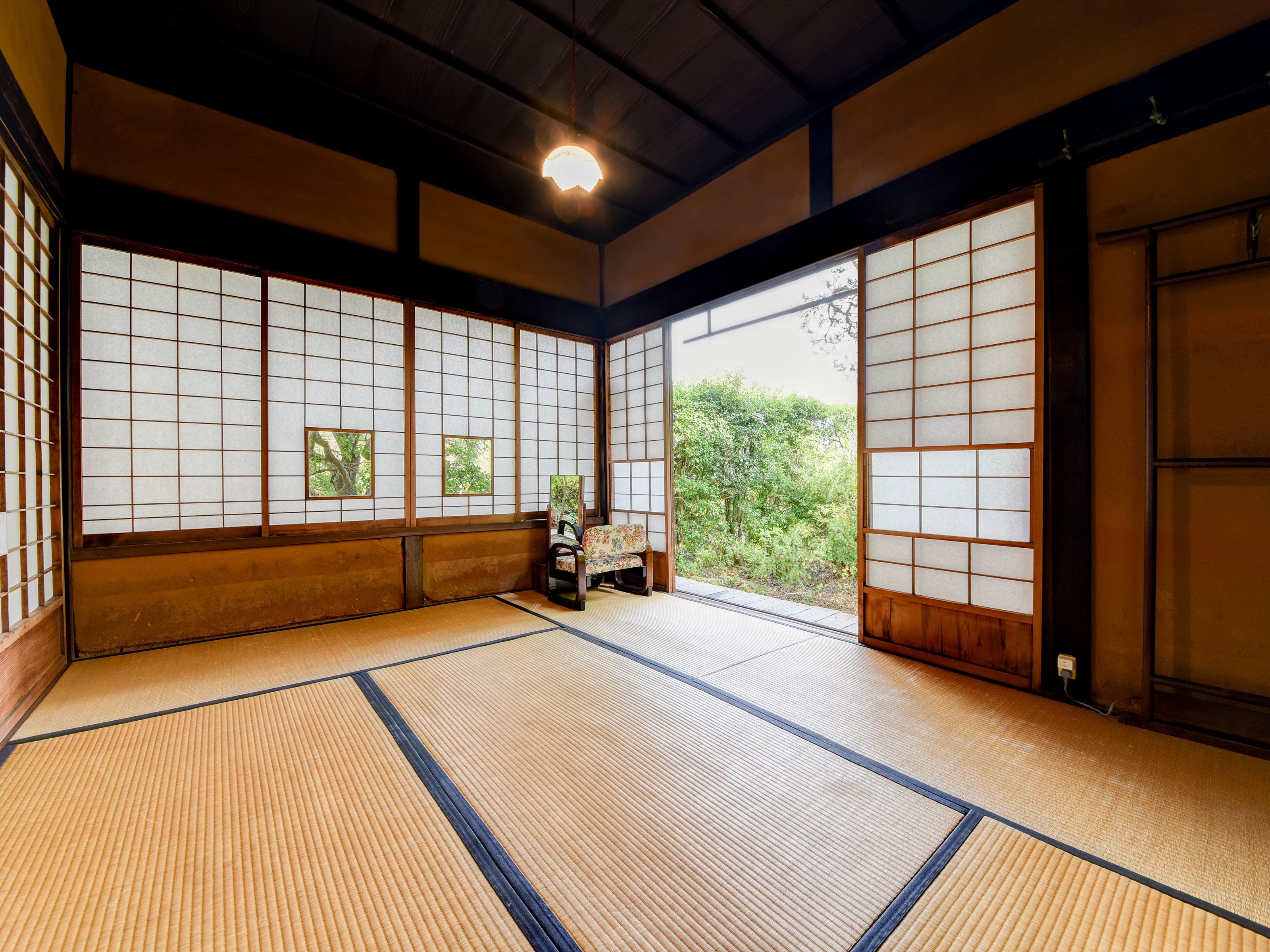A traditional Japanese room with tatami flooring, shoji screens, and a view of greenery outside.