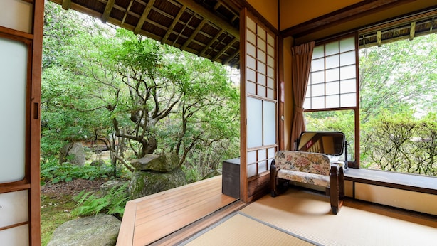 Una habitación japonesa tradicional con suelo de tatami, un banco de madera y vistas a un jardín exuberante a través de puertas correderas.