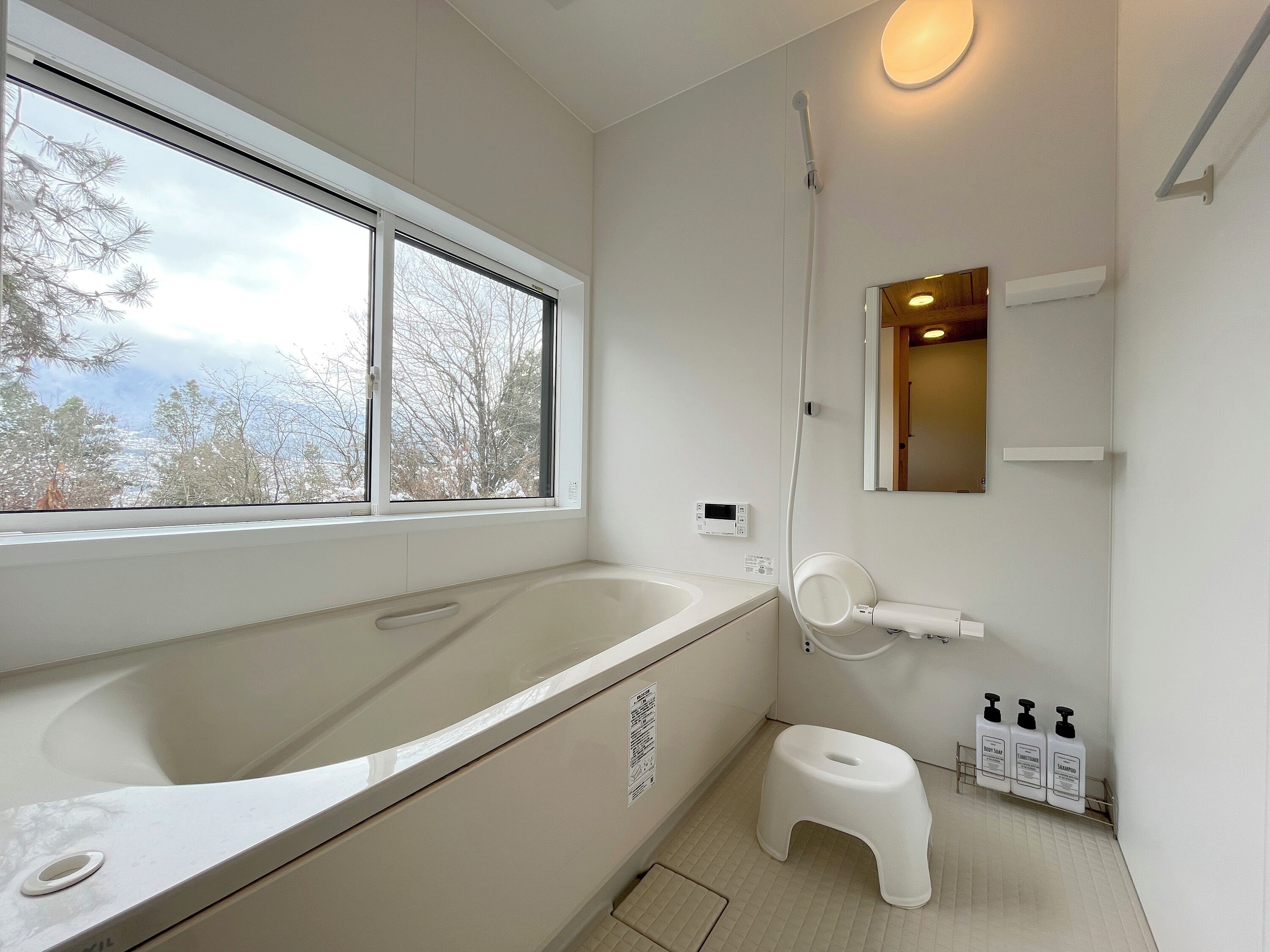 A bathroom with a bathtub, a toilet, a shower, and a window with a view of trees.