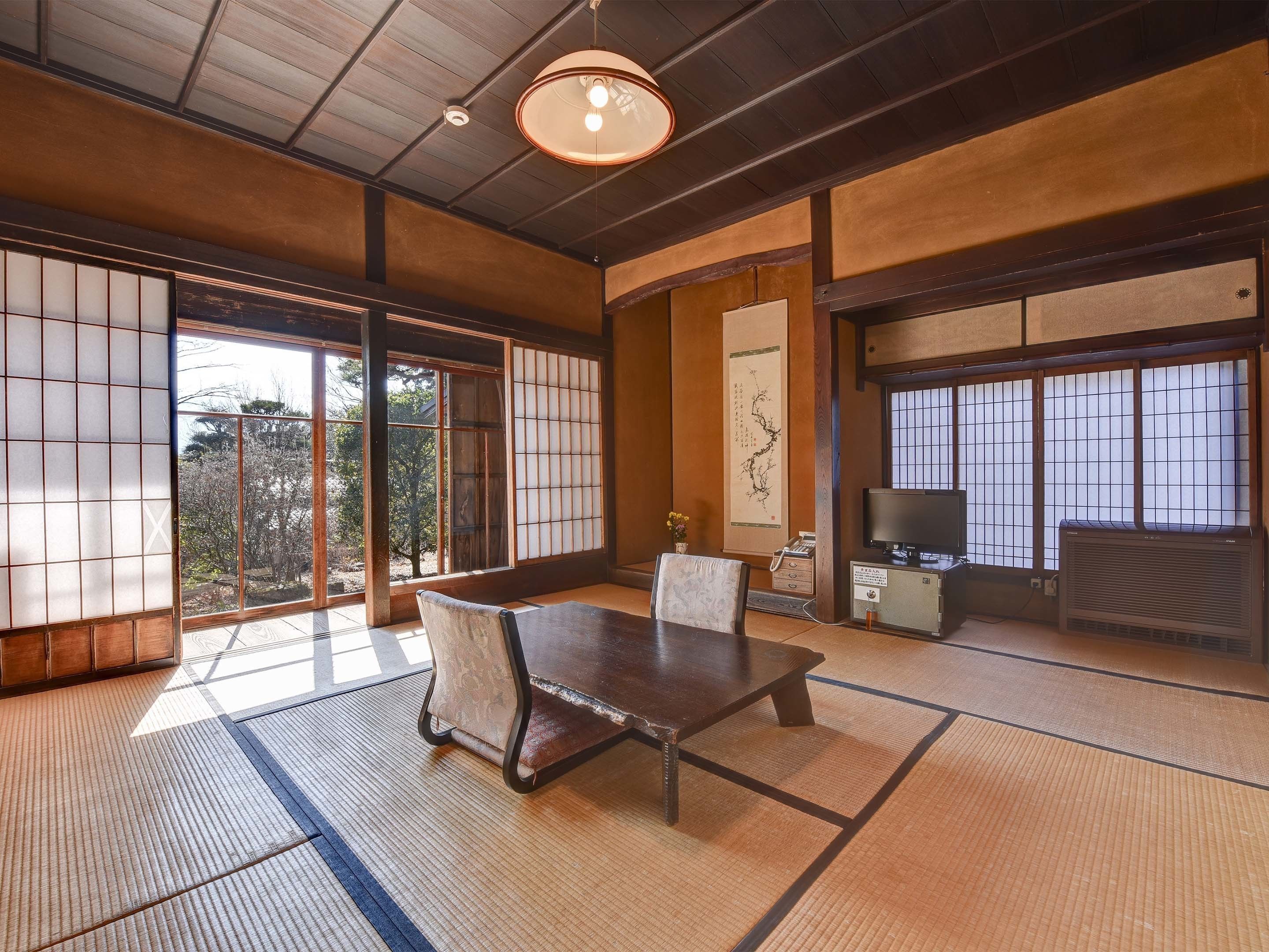 Ett traditionellt japanskt rum med tatamimattor på golvet, ett lågt bord, stolar, en tv och skjutdörrar med shojipaneler.