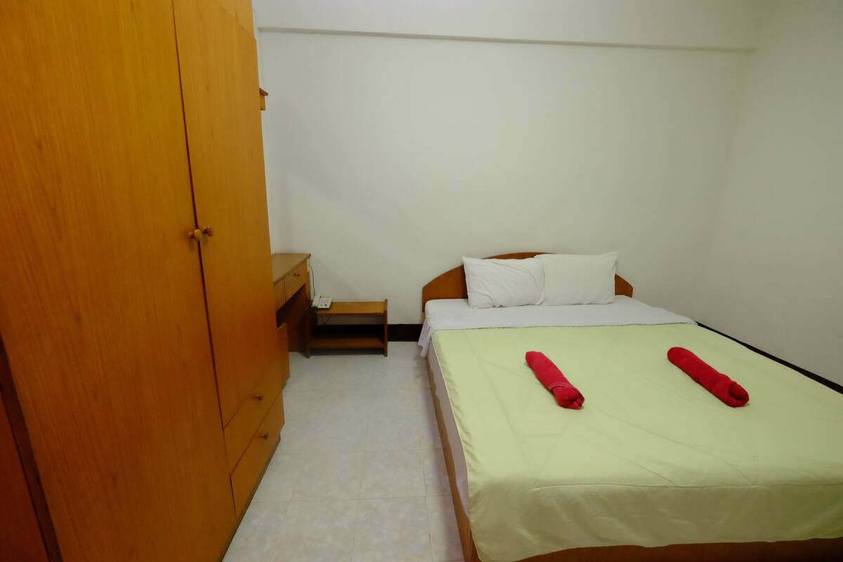 A small, clean room with a bed, a wooden wardrobe, and a nightstand.