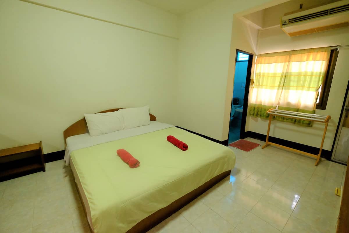 A room with a bed, a wooden bench, a small table, and a window with curtains.