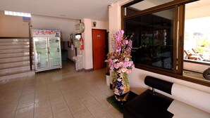 Un hall de hotel con refrigerador, un jarrón de flores, un banco y un ventanal grande.