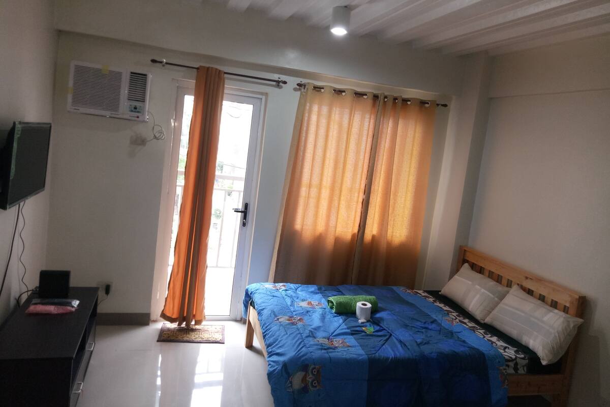 A room with a bed, a desk, a television, and a window with curtains.