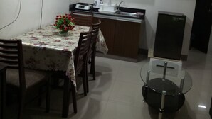 Een kleine keuken met houten kastjes, een eettafel met stoelen, een kleine koelkast en een flatscreen televisie aan de muur.
