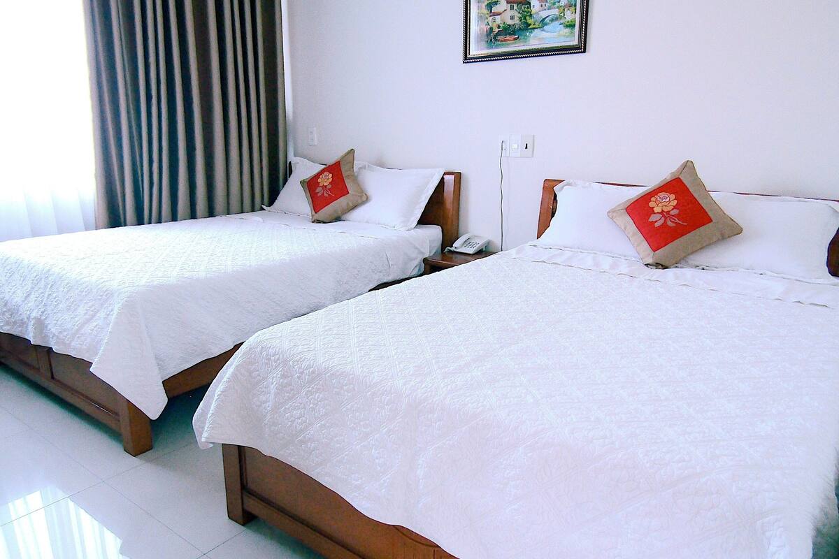 Dos camas individuales con ropa blanca y almohadas decorativas rojas, un teléfono en la mesita de noche y un enchufe en la pared.